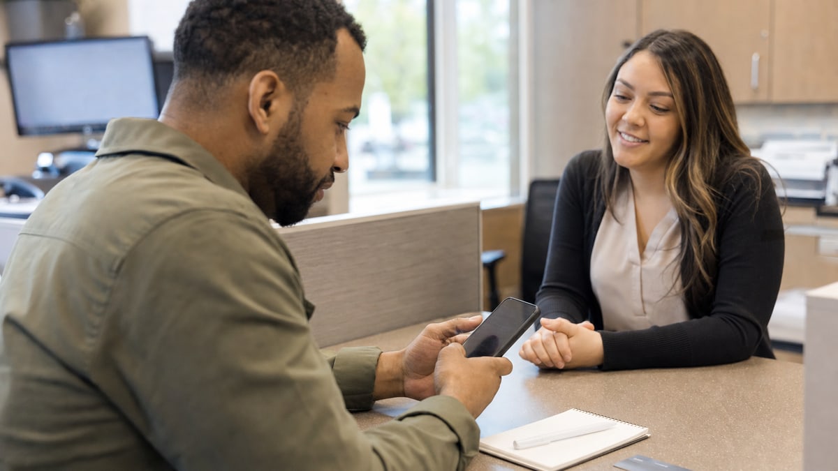 A consumer reviewing a credit card payoff plan on a phone at a credit-union counter.